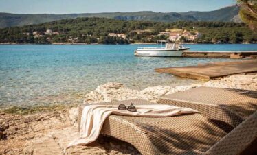 Relaxing lakeside scene with sun loungers and boat in the background.