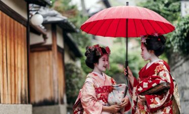 Two women in traditional Japanese kimonos sharing an umbrella outdoors.