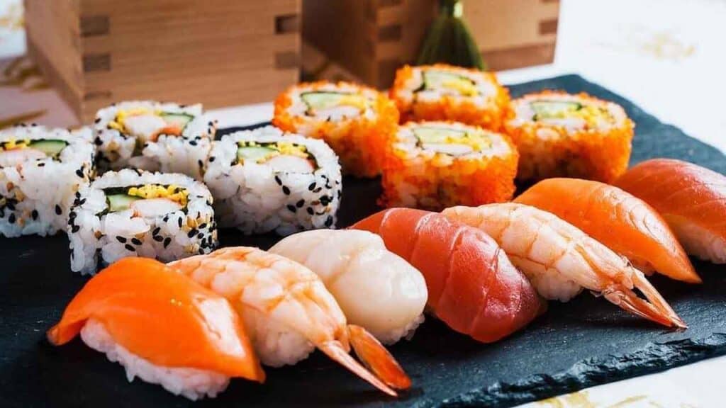 Delicious sushi assortment featuring fresh salmon nigiri and colourful sushi rolls on a black slate.