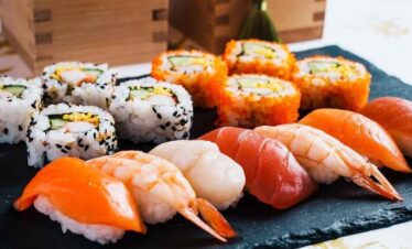 Delicious sushi assortment featuring fresh salmon nigiri and colourful sushi rolls on a black slate.