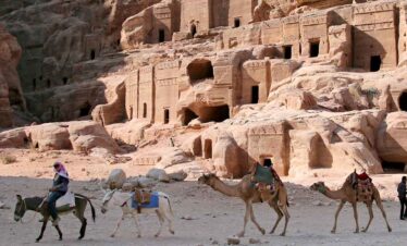 Camels and tourists exploring ancient tombs in a desert landscape.