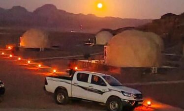 Sunset over desert camp with dome-shaped tents and a white pickup truck in the foreground.