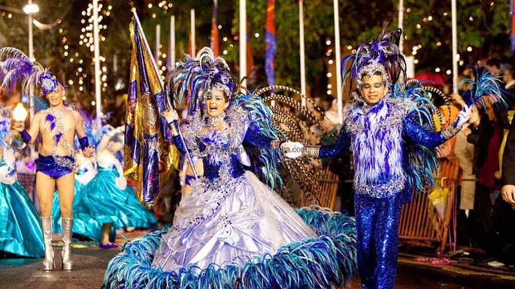 An energetic carnival parade featuring performers in colourful, elaborate costumes with feathers and.