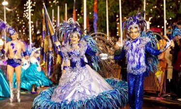 An energetic carnival parade featuring performers in colourful, elaborate costumes with feathers and.