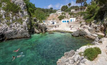 A small cove with turquoise waters, rocky cliffs, and white buildings in a scenic coastal area.