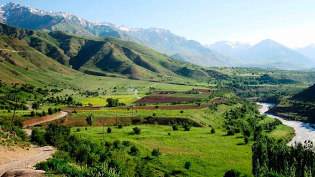 An expansive view of lush green valleys with rolling hills and distant mountain peaks under a clear.
