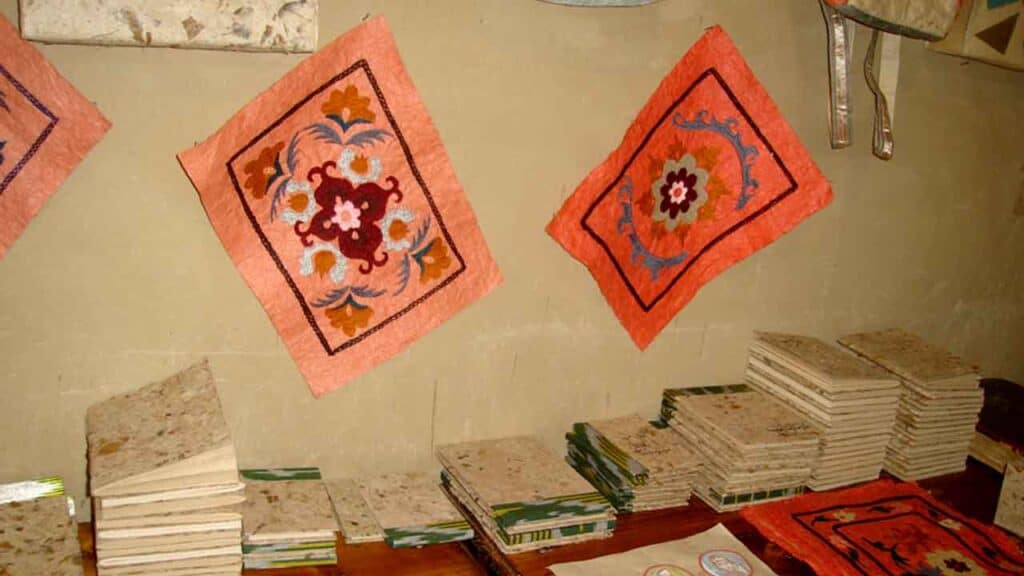 Colourful patterned rugs hanging on a wall with stacks of tiles below.