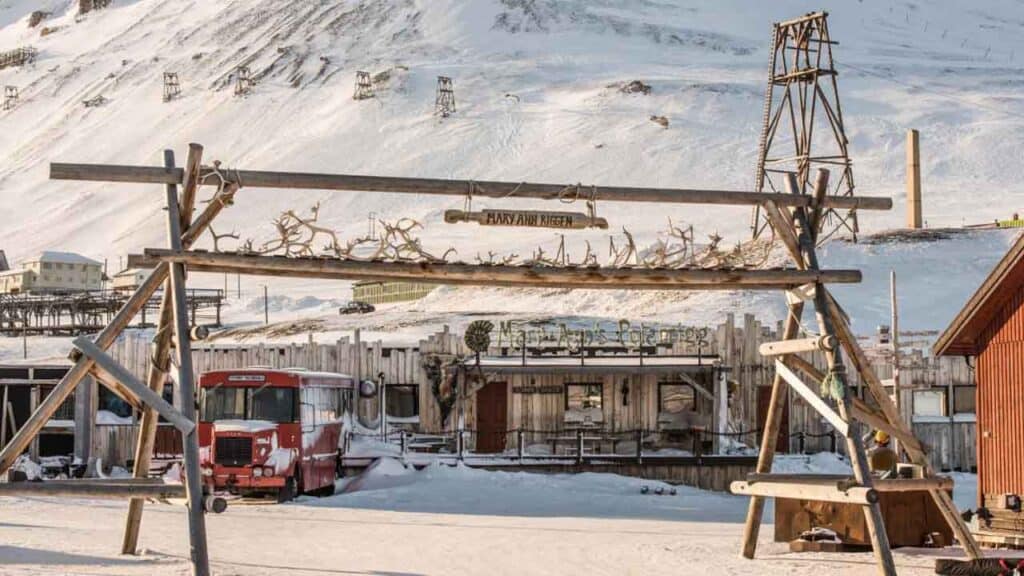 Snow-covered mountain village with rustic buildings and vintage vehicles.