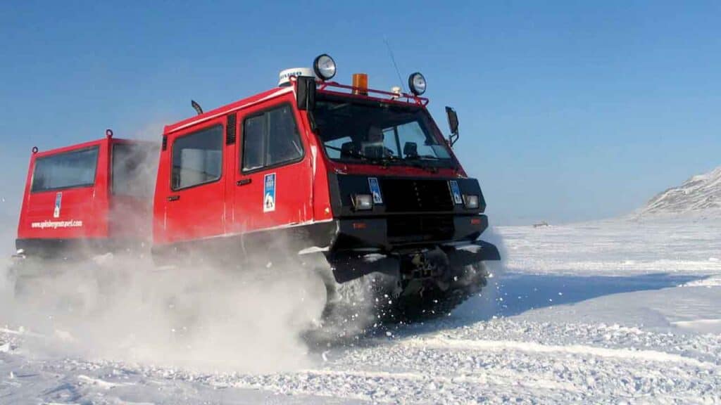 Red snowcat vehicle driving across snowy landscape in winter.