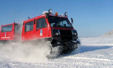 Red snowcat vehicle driving across snowy landscape in winter.