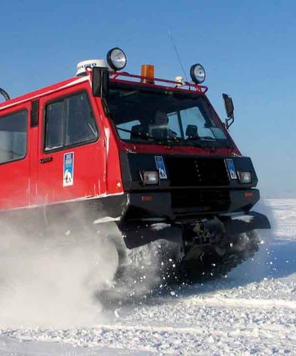 Red snowcat vehicle driving across snowy landscape in winter.