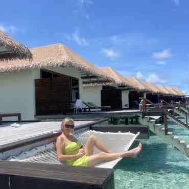 Overwater bungalow with a woman relaxing on a hammock in the water, tropical resort setting, clear b.