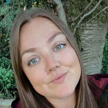 Relaxed woman with blue eyes and long brown hair in a natural outdoor setting.