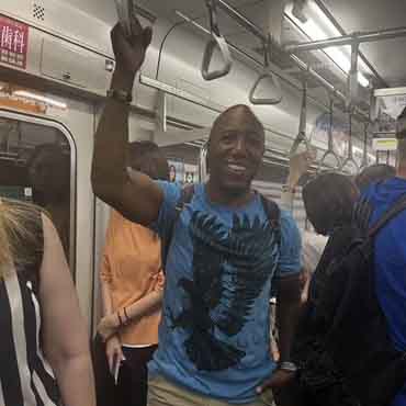An excited man smiling and waving while riding a bus with fellow travellers.