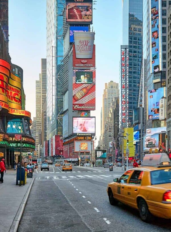 Bright Times Square with billboards and yellow taxi.