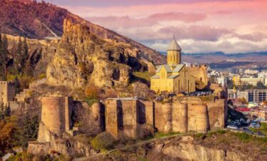 Ancient fortress ruins with a church on a hill overlooking Tbilisi at sunset.