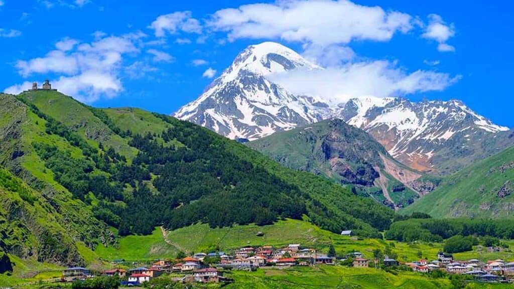 Capped mountain with green hills and a small village at the base.