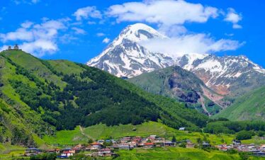 Capped mountain with green hills and a small village at the base.
