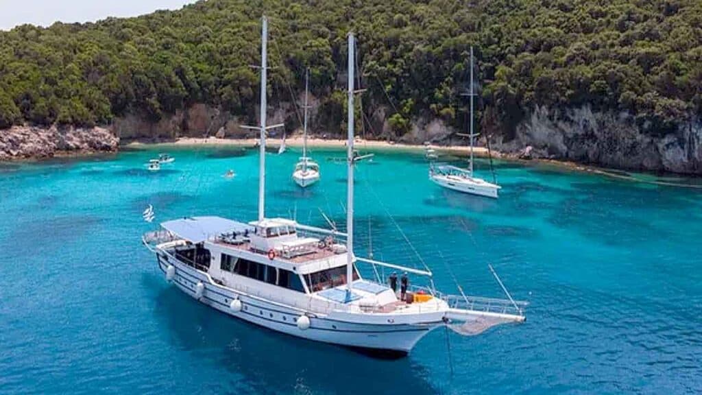 Elegant yacht sailing in turquoise waters near lush green coastline.