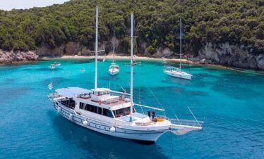 Elegant yacht sailing in turquoise waters near lush green coastline.