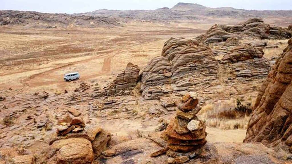 Scenic desert landscape with rock formations and a camper van in the distance.