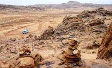 Scenic desert landscape with rock formations and a camper van in the distance.