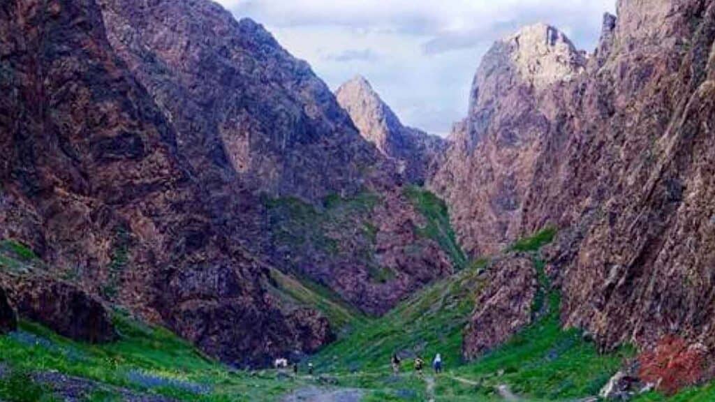 Scenic mountain valley with hikers exploring rugged terrain and lush greenery.