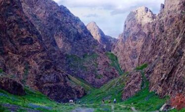 Scenic mountain valley with hikers exploring rugged terrain and lush greenery.