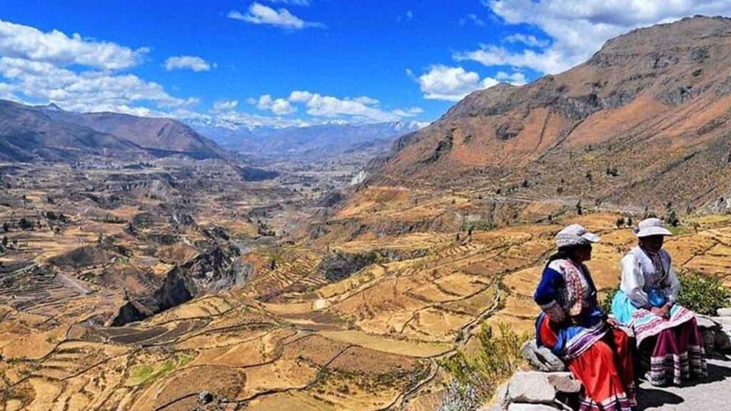 Two women in traditional clothing sitting in the Andes mountains.