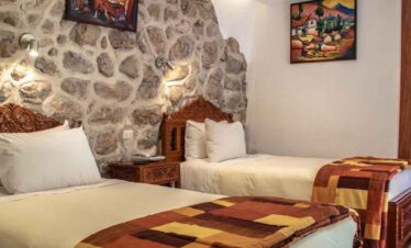 Bright hotel room with two single beds and colourful artwork on stone wall background.