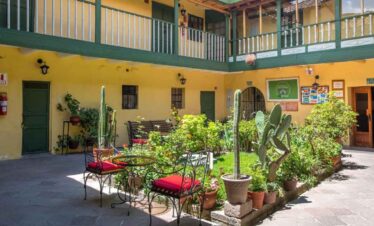 Courtyard with outdoor seating and lush plants at Travel Buddies Holidays hostel in a colourful buil.