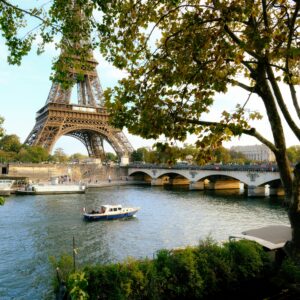 Eiffel Tower view over the Seine River with boats and trees in Paris.