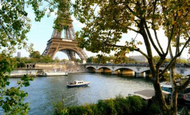 Eiffel Tower and Seine River scene with boats and trees in Paris, France.