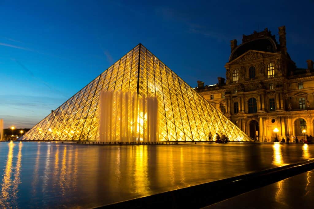 Paris Louvre Pyramid illuminated at night with reflections in water.