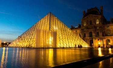 Paris Louvre Pyramid illuminated at night with reflections in water.