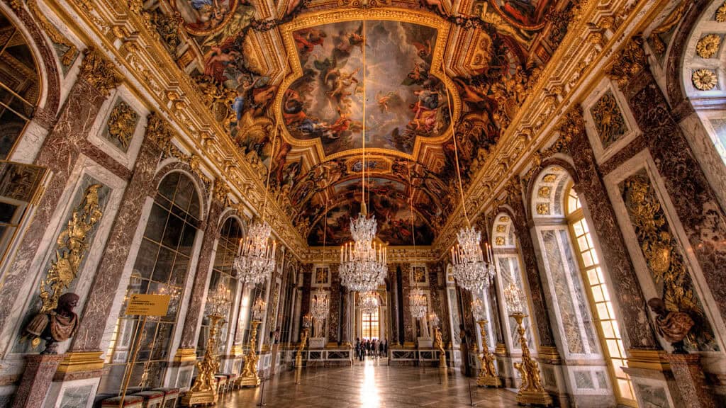 Elegant Palace of Versailles grand hall with ornate gold details and stunning ceiling frescoes.