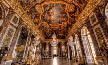 Elegant Palace of Versailles grand hall with ornate gold details and stunning ceiling frescoes.