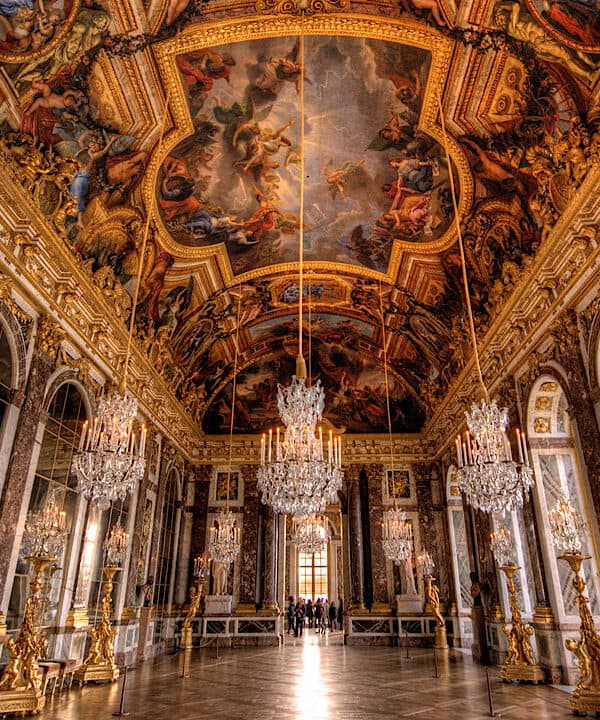 Elegant Palace of Versailles grand hall with ornate gold details and stunning ceiling frescoes.